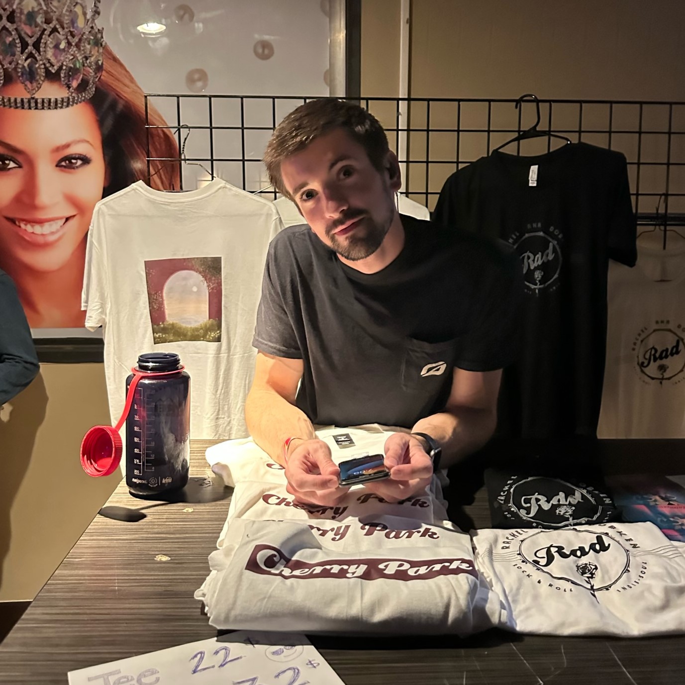 Band member standing behind merchandise table, looking at the camera